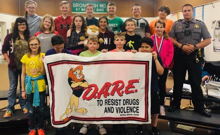 Group picture with the D.A.R.E class. The children in the front are holding a sign reading 'D.A.R.E to resist drugs and violence.'
